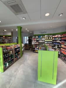Travaux de rénovation de l'espace client d'une pharmacie avec meubles gondole en bois vert, étagères murales pour les médicaments et signalétique